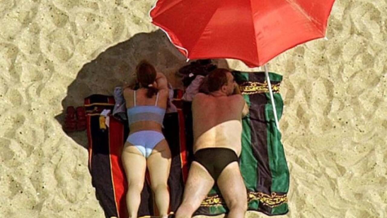 Ein Paar geniesst unter einem Sonnenschirm liegend den Sandstrand Ein Paar geniesst unter einem Sonnenschirm liegend den Sandstrand