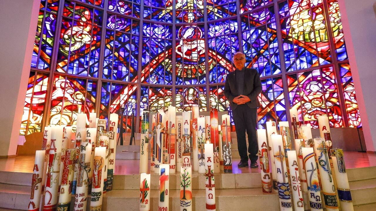 Alois Dürlinger in der Salzburger Stadtpfarrkirche Herrnau inmitten der Osterkerzen aus 29 Jahren als Pfarrer. Das 320 Quadratmeter große Glasfenster ist eines der größten in Europa.  