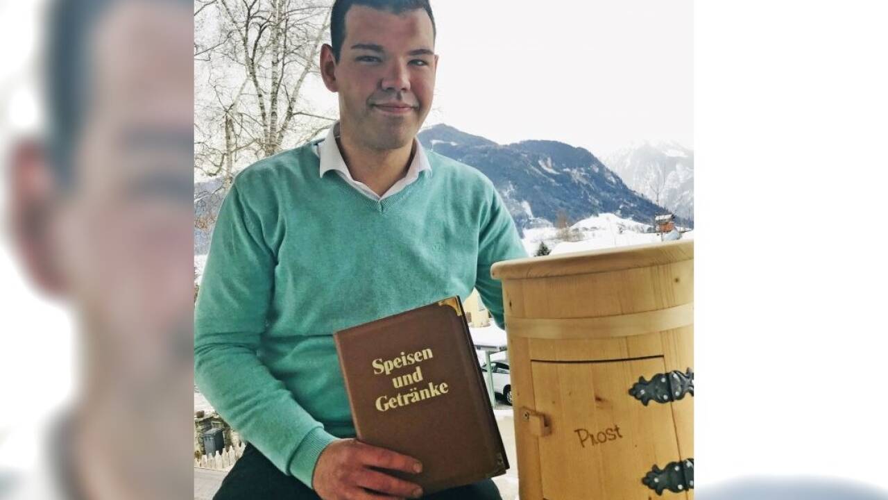 Zu Hause auf dem Balkon: der junge Wirt mit der bewährten Speisekarte. Und mit einem Hocker, der in seinem Inneren eine Schnapsflasche und Stamperl versteckt hält– ein Geburtstagsgeschenk.  
