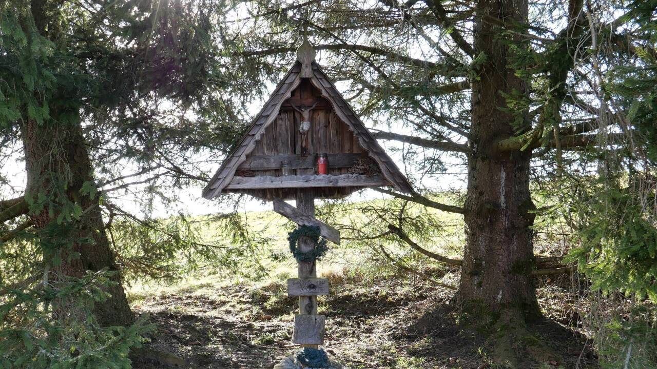 Unter zwei mächtigen Fichten duckt sich das Kreuz.  