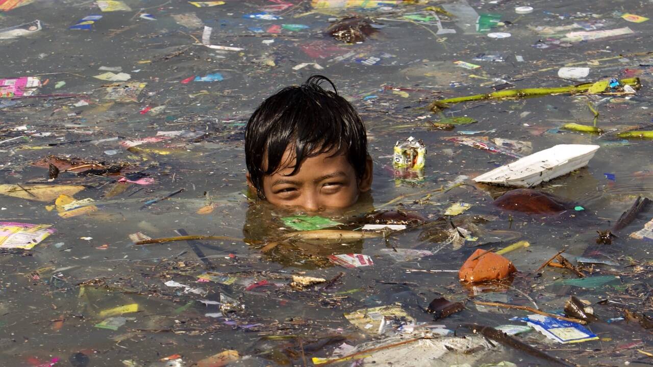 Ein Bub aus Manila schwimmt in Zivilisationsmüll - ein Sinnbild für den Zustand des Planeten.  Ein Bub aus Manila schwimmt in Zivilisationsmüll - ein Sinnbild für den Zustand des Planeten.