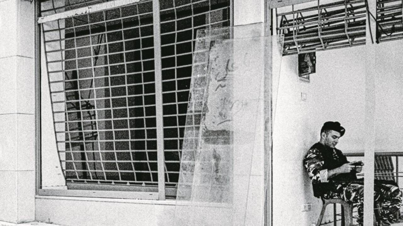 Soldat spielt am Handy, Sturmgewehr am Schoß, vor geplünderten Auslagen im Zentrum von Beirut. 