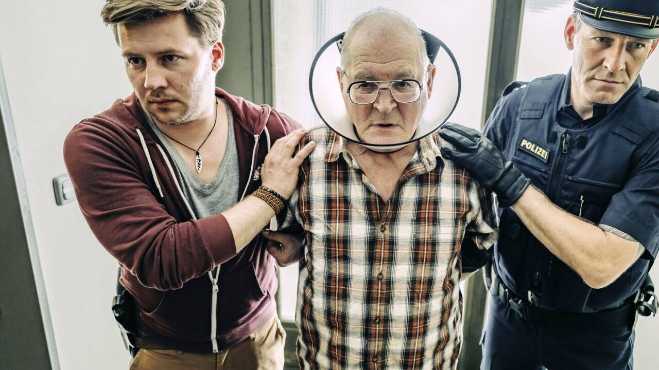 Der Querulant Hackl (Burghart Klaußner) wird von zwei Polizisten unter besonderen Schutzmaßnahmen abgeführt. 