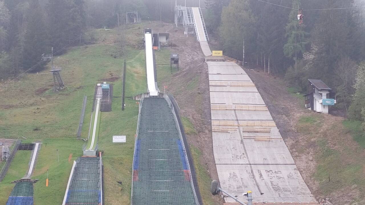 Die Arbeiten an der Großschanze rechts laufen, aber nicht ohne Schwierigkeiten. Die kaputte Zufahrt führt von oben durch den Wald zum Anlaufturm. 