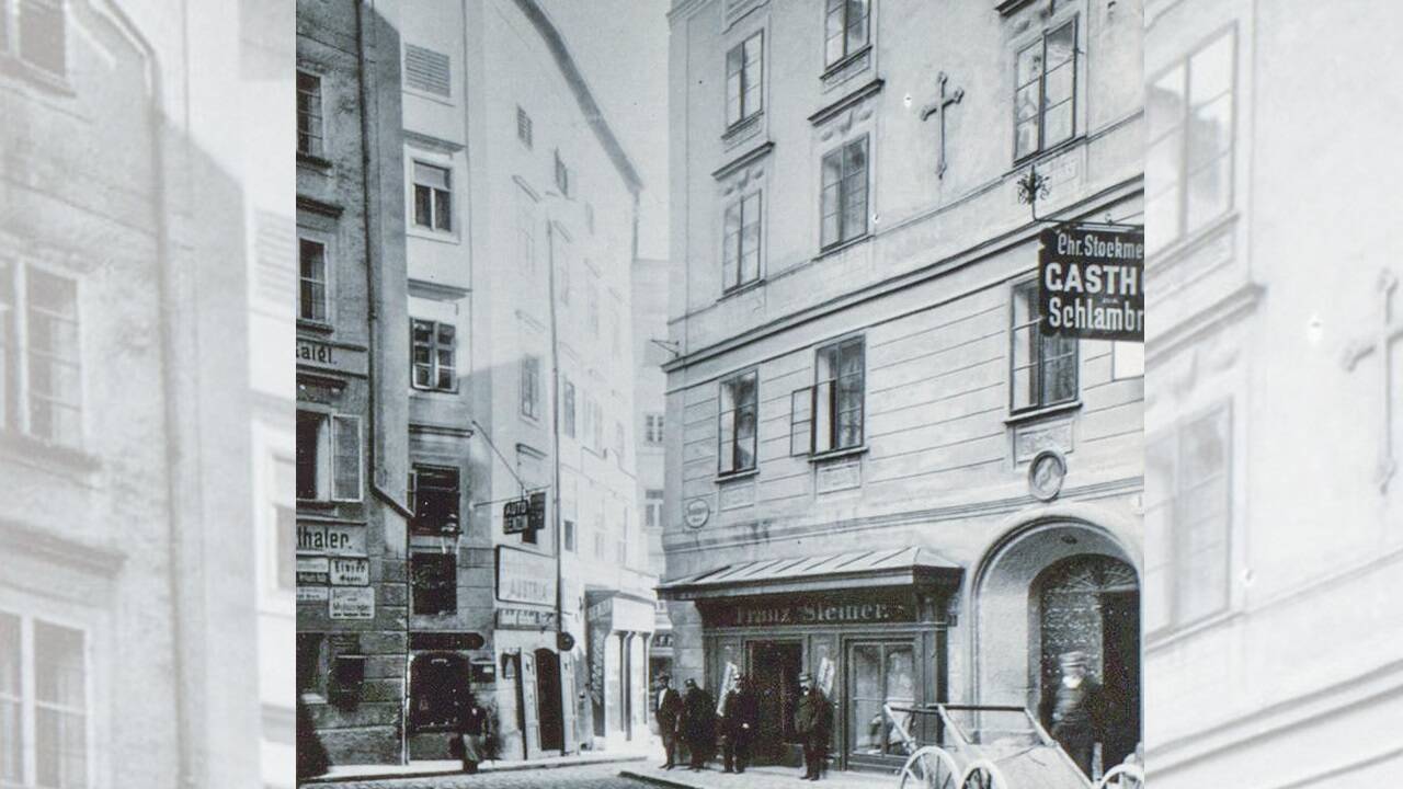 Das Wirtshausschild des Gasthofs „Schlambräu“, damals im Besitz von Christoph Stockmeyer, aufgenommen in Blickrichtung Platzl im Jahr 1906. Im anschließenden ehem. Wirtshaus „Goldenes Kreuz“ in der Dreifaltigkeitsgasse 1 hatte der Tischler Franz Steiner sein Geschäft. Das „Zellereck“ genannte Gebäude wurde 1908 abgebrochen. 