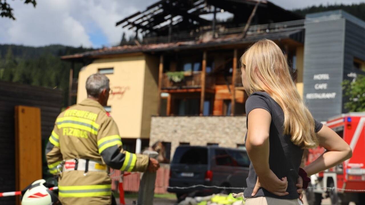Eine Urlauberin und ein Feuerwehrmann vor dem schwer beschädigten Neubergerhof in Filzmoos. 