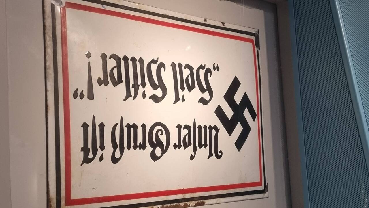 Das Schild hängt in der Dauerausstellung „Idyll und Verbrechen' absichtlich verkehrt herum in der Ausstellung. Es ruft so eine Irritation bei den Besuchenden hervor und macht ein potenzielles 'Selfiemotiv' für Personen mit rechtem oder rechtsextremem Gedankengut unattraktiv.  