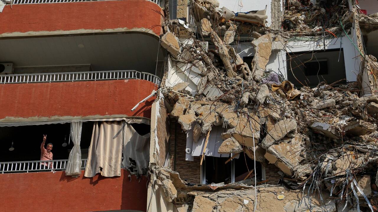 Ein Rückkehrer deutet vom Balkon seiner Wohnung in Tyre. Das Gebäude daneben wurde schwer getroffen.  Ein Rückkehrer deutet vom Balkon seiner Wohnung in Tyre. Das Gebäude daneben wurde schwer getroffen.