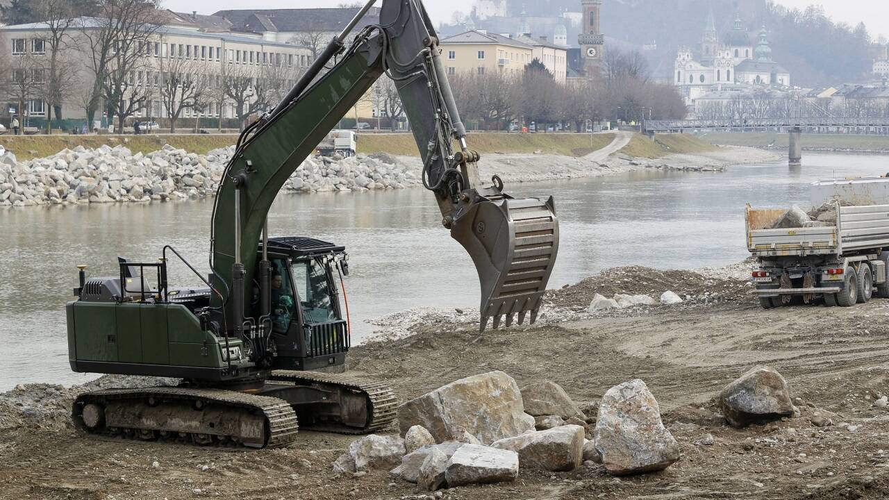 Bagger und Lkw sind auf der Sandbank in der Salzach im Einsatz. Es gilt, schwere Fracht an die richtigen Stellen zu befördern.  
