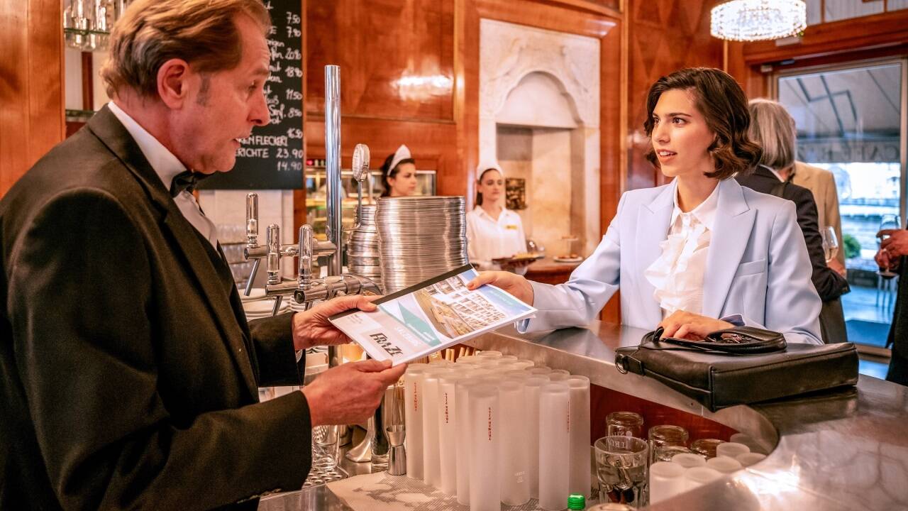 Im Café Bazar: Helmut Bohatsch als Ober Herr Wolfgang und Laura Euler-Rolle als Immobilienmaklerin Noelle Imlauer.  