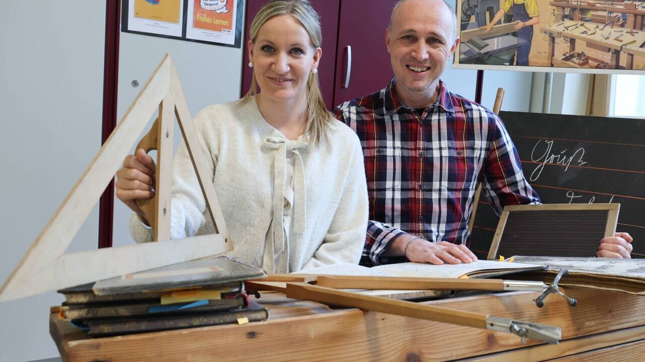 Jacqueline Huber, Leiterin der Volksschule Maxglan 2, und Gerhard Wildling, Leiter der Volksschule Maxglan 1, an einem historischen Schulpult. Die beiden haben eine Schulchronik geschrieben und eine Ausstellung gestaltet.  