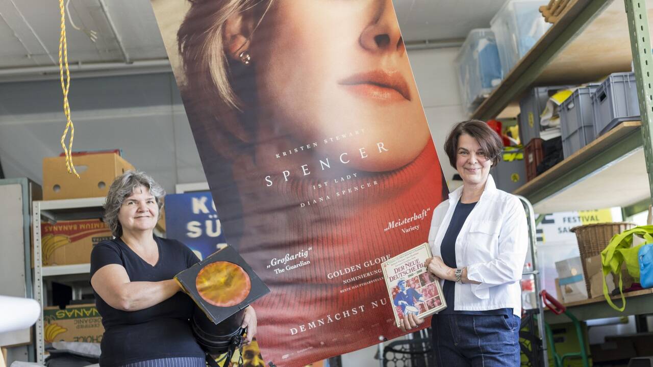 Geschäftsführerin Renate Wurm und Mitarbeiterin Irmi Költringer vor einem der Filmtransparente, die bei dem Flohmarkt verkauft werden. Auch alte Scheinwerfer und Bücher sind im Angebot.  