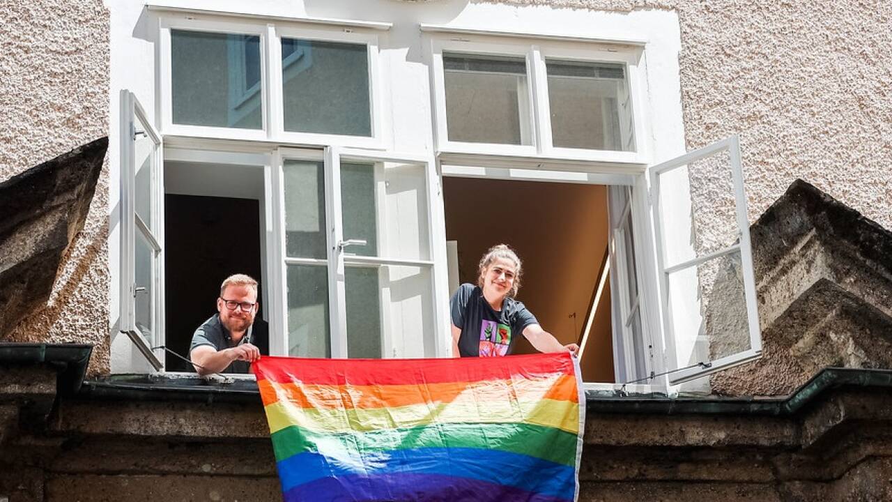 Natalie Hangöbl und Markus Walter mit der Regenbogen-Flagge über dem Eingangsportal des Chiemseehofs.  