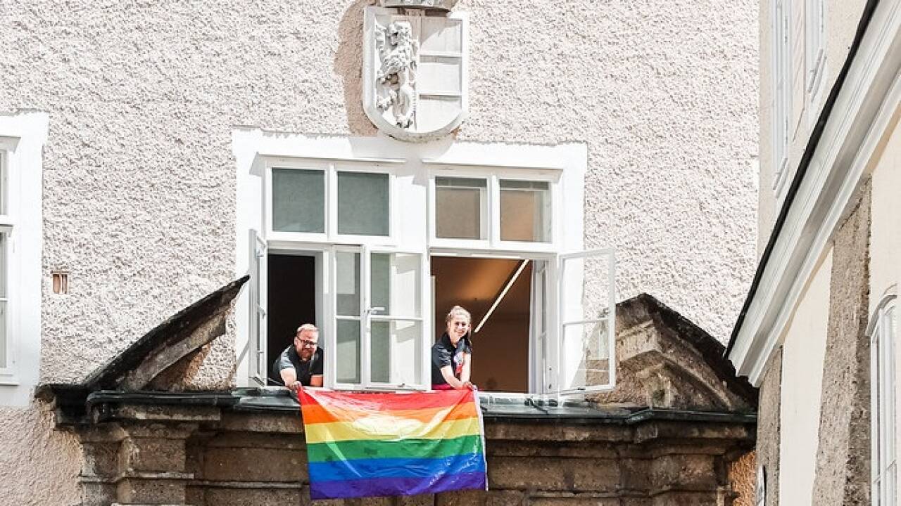 Natalie Hangöbl und Markus Walter mit der Regenbogen-Flagge über dem Eingangsportal des Chiemseehofs.  