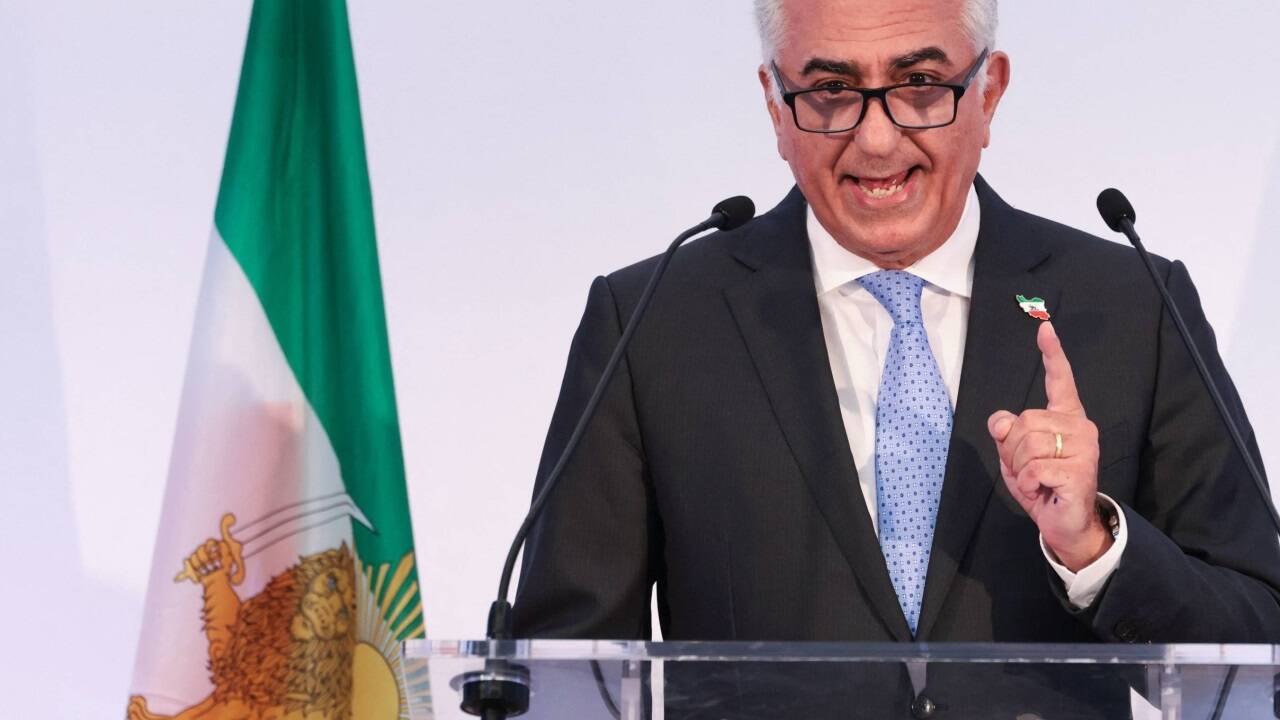 Reza Pahlavi bei der Pressekonferenz vor der ehemaligen iranischen Flagge mit Löwe und Sonne. 