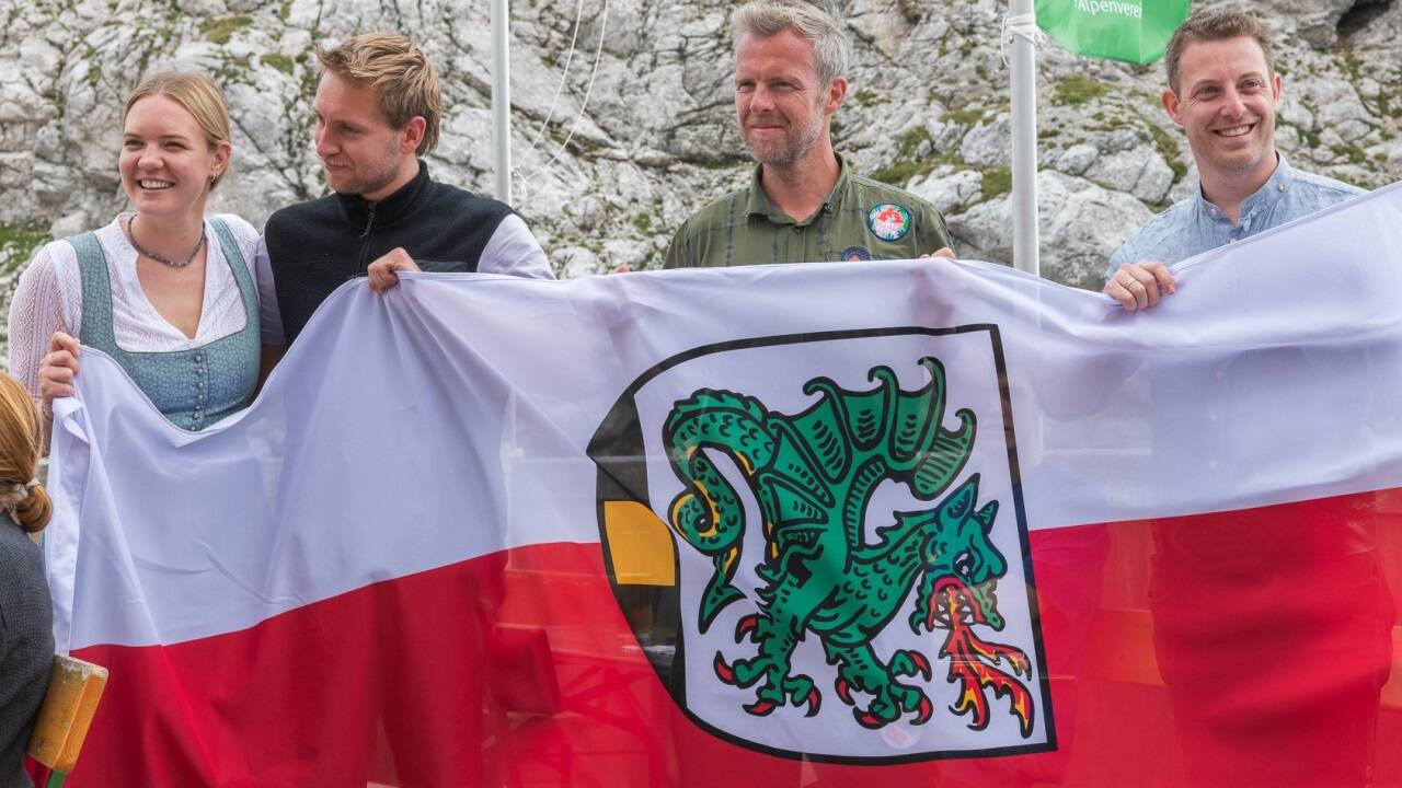 Die Fahne zeigt das Maria Almer Wappen. V. l.: die Hüttenwirtsleute Laura Heiligensetzer und Jeremy Aicher, Sepp Schwaiger (TVB Hochkönig) und Vizebürgermeister Dominik Struber.  