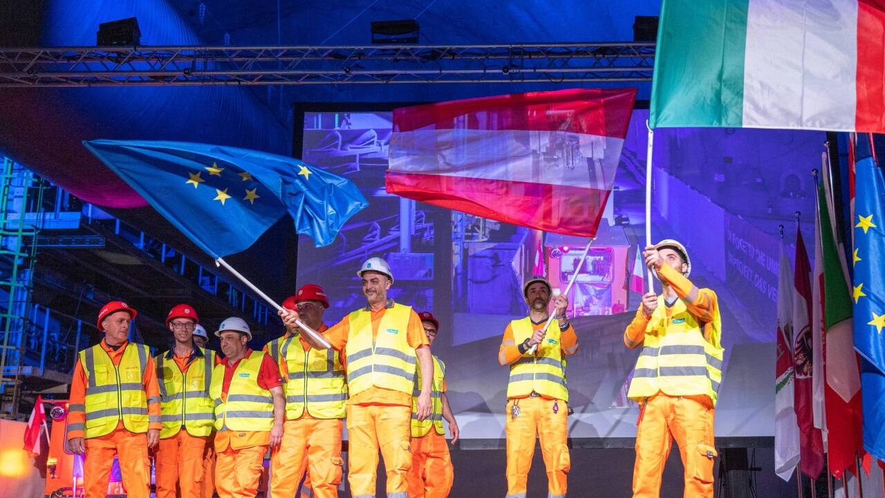 Mitarbeiter der BBT SE schwingen die Flaggen der EU, Österreichs und Italiens anlässlich der Ankunft der Tunnelbohrmaschine Virginia am Brenner am 30. März 2023 im Tunnel Mauls (Südtirol). 