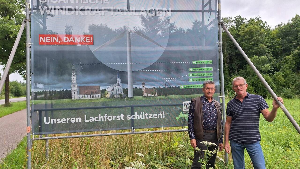 Norbert Labmayer und Harald Neuburger (r.) vor ihrem Aktionsplakat, das den Höhenvergleich des „Riesenrads“ mit den Kirchen von Braunau, Neukirchen an der Enknach und Burgkirchen zeigt. 