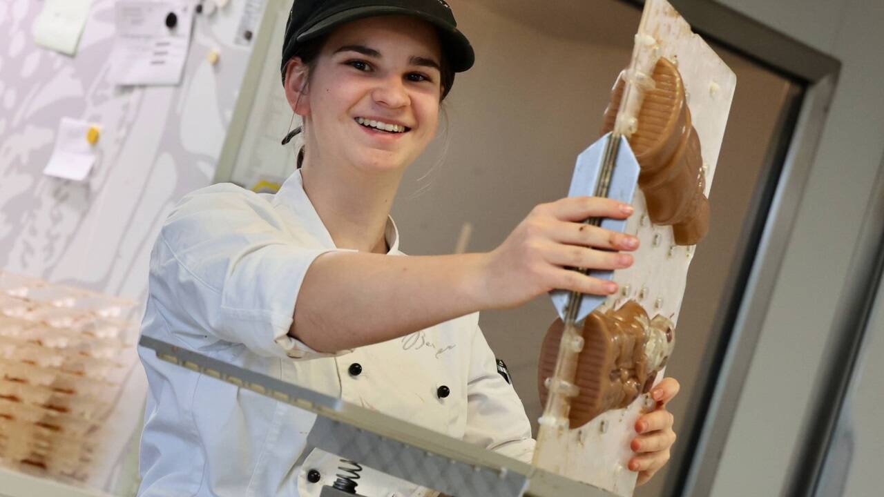 Damit sich die Schokolade gleichmäßig verteilt, schwenken Mitarbeiterinnen die Formen in alle Richtungen. Mithilfe einer Rüttelplatte verschwinden kleine Luftbläschen. 