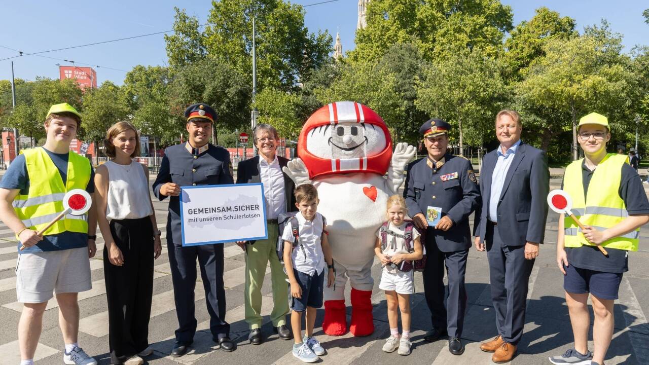 Von links nach rechts: Dipl.-Ing. Klaus Robatsch, Leiter des Bereichs Verkehrssicherheit im KFV; Bundespolizeidirektor Michael Takács, BA MA MSc; Mag. (FH) Roland Pichler, Generaldirektor-Stv. der AUVA; mit Sicherheitsmaskottchen HELMI, 2 Schülerlotsen und Schulkindern. 