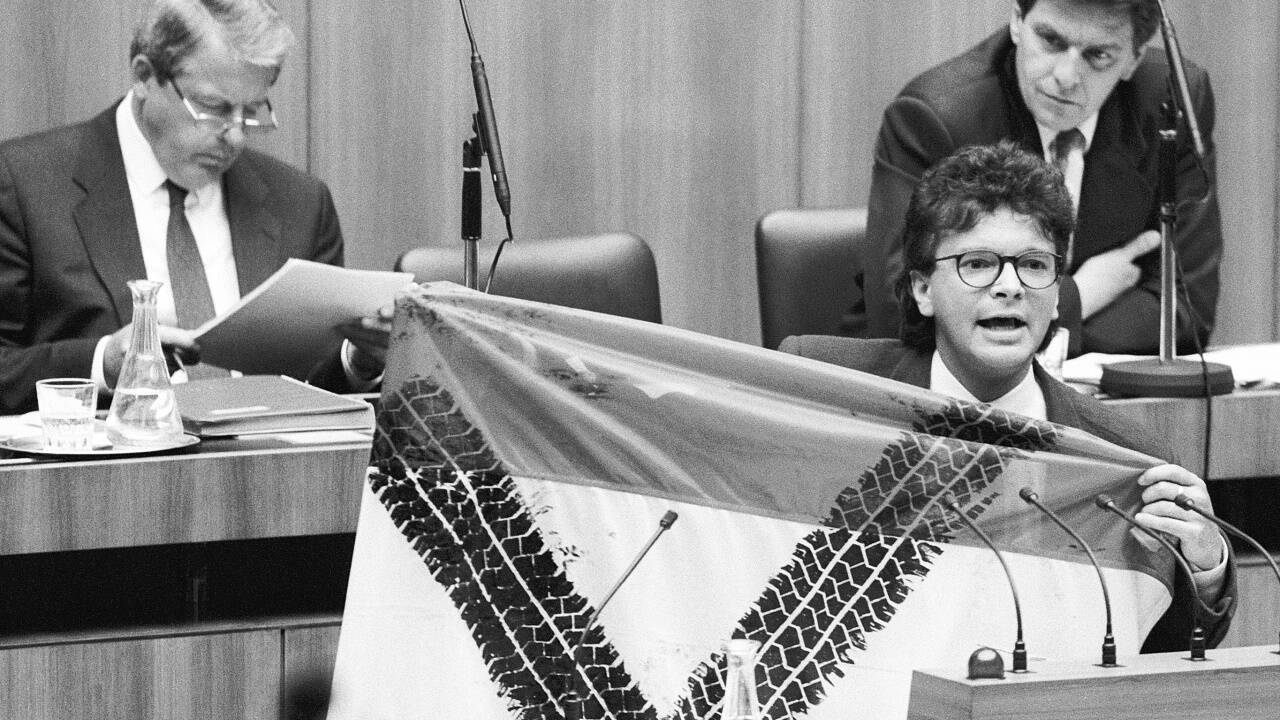 Die Grün-Alternativen brachten am 12. Mai 1992 einen Misstrauensantrag gegen Bundeskanzler Franz Vranitzky im Zusammenhang mit dem Transitvertrag mi der EG ein. Auf dem Bild: der Grüne Abgeordnete Rudi Anschober mit einer österreichischen Fahne, durchkreuzt von Reifenspuren - im Hintergrund Bundeskanzler Franz Vranitzky und Verkehrsminister Viktor Klima. 