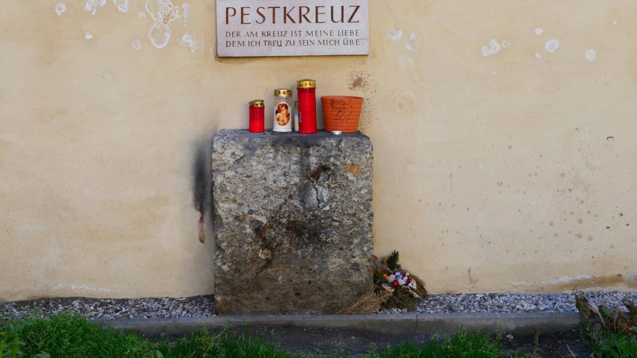 Die Inschrift über dem Steinsockel mit den Kerzen.  