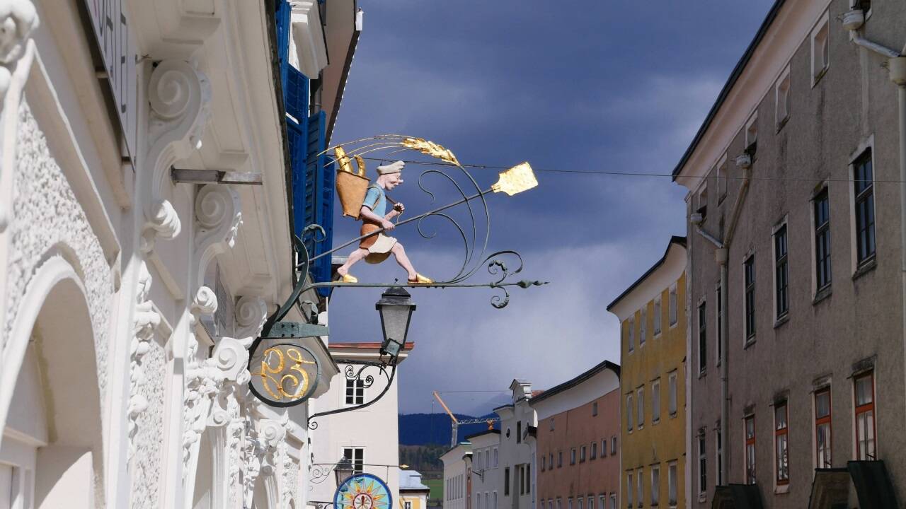 Blick auf das Bäckerzeichen am Oberen Markt in Hallein, im Hintergrund das Hauszeichen der ehemaligen Glaserei J. Alfarè.  