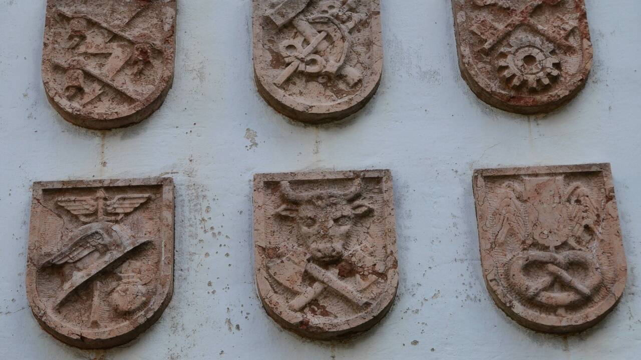 Detailaufnahme der Zunftzeichen, darunter für den Schlosser (zwei gekreuzte Schlüssel mit Zahnrad), den Bäcker (Brezel) und Metzger (Stierkopf und Beil).  