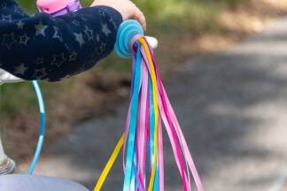  Bunte Bänder für die Griffe: Bunte Bänder in der Mitte falten und mit der Schlaufe durch einen kleinen Haargummi fädeln. Bänder um den Gummi durch die Schlaufe festziehen. Gummibänder am Lenker befestigen und losdüsen.<br /> 